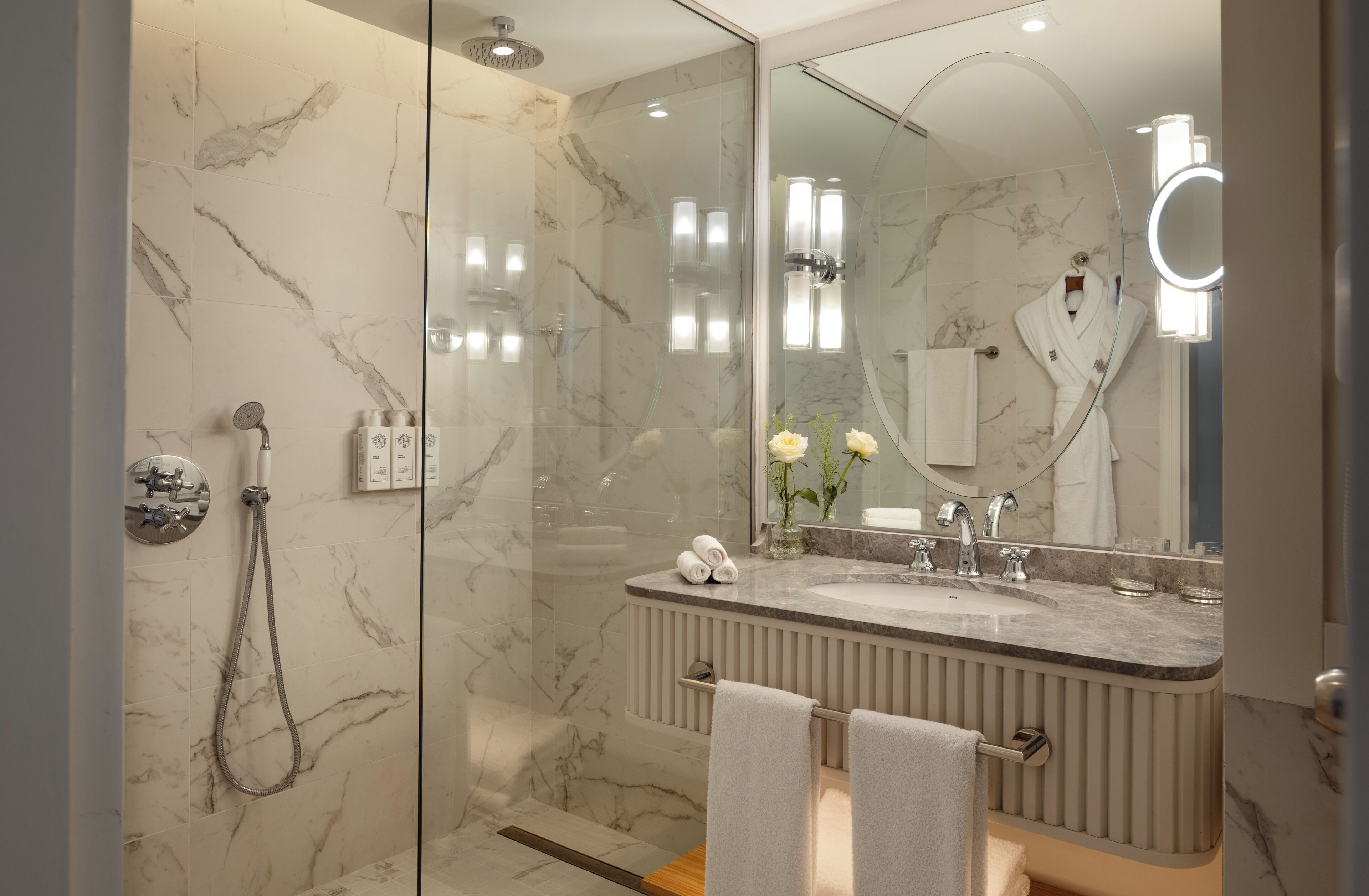 Une salle de bain moderne avec une douche à parois de verre, un mur recouvert de carreaux de marbre, un meuble-lavabo et un grand miroir.