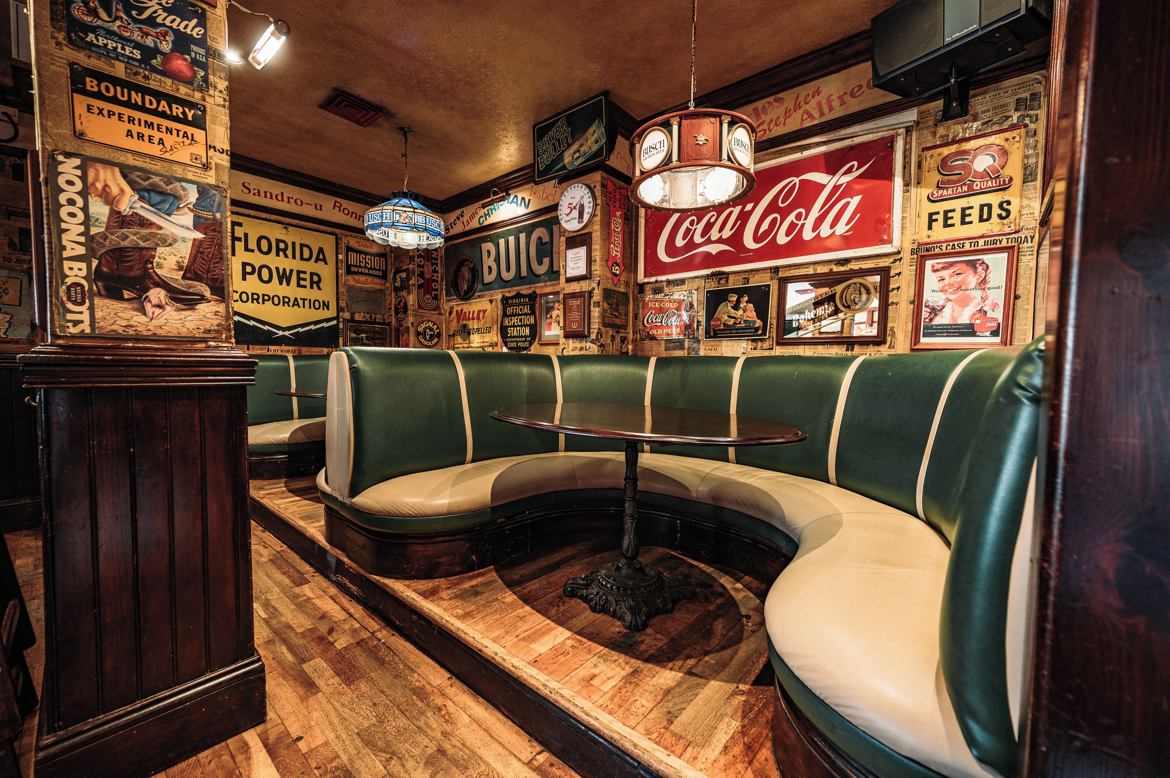A vintage diner interior with green booths, a wooden floor, and vintage advertisements on the walls.