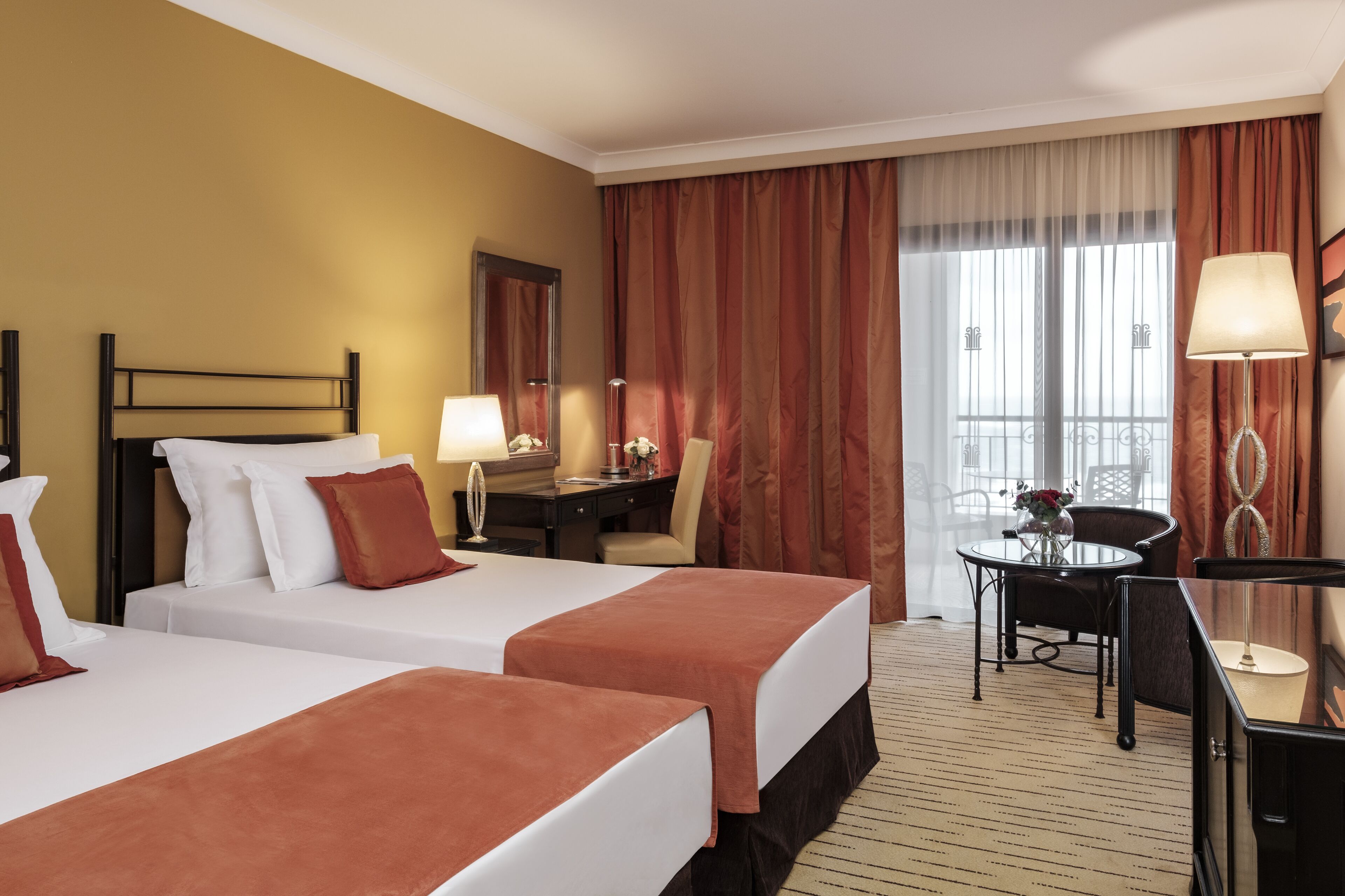 Une chambre d’hôtel avec deux lits, un bureau, une chaise et un balcon avec des rideaux.