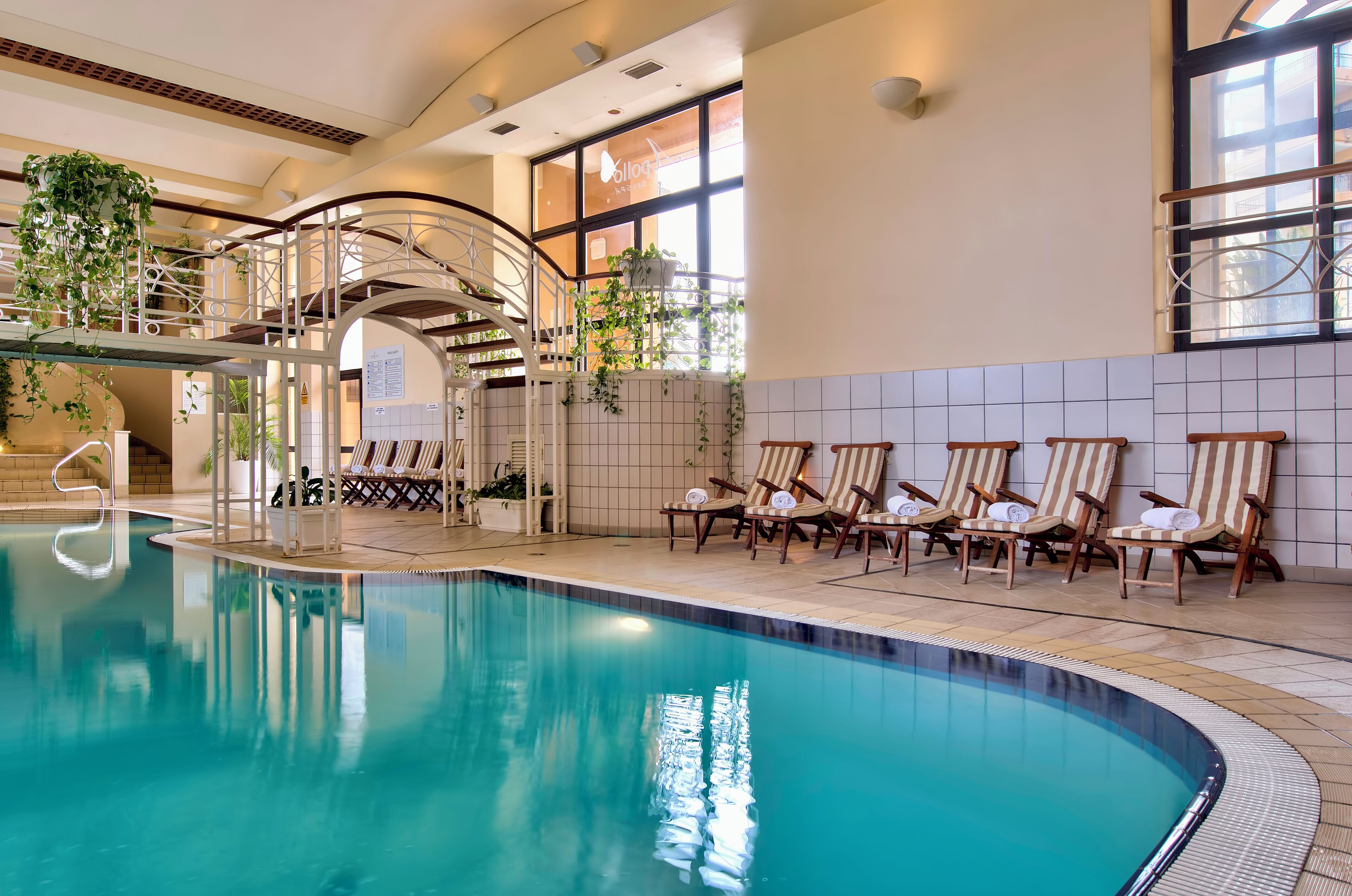 A swimming pool with lounge chairs and a covered seating area with plants.