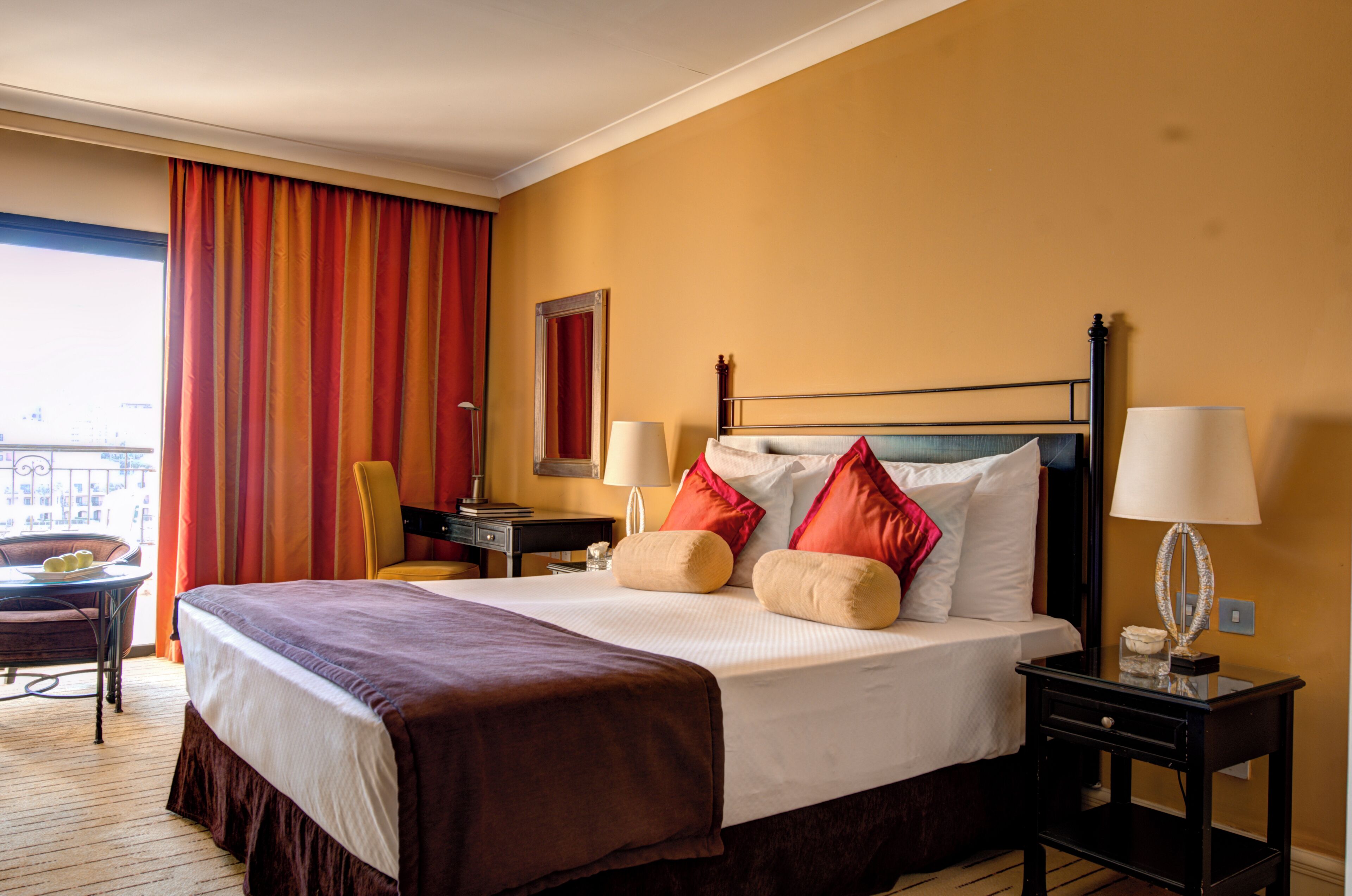 A hotel room with a large bed, two bedside tables, a chair, a desk, and a view of the city.