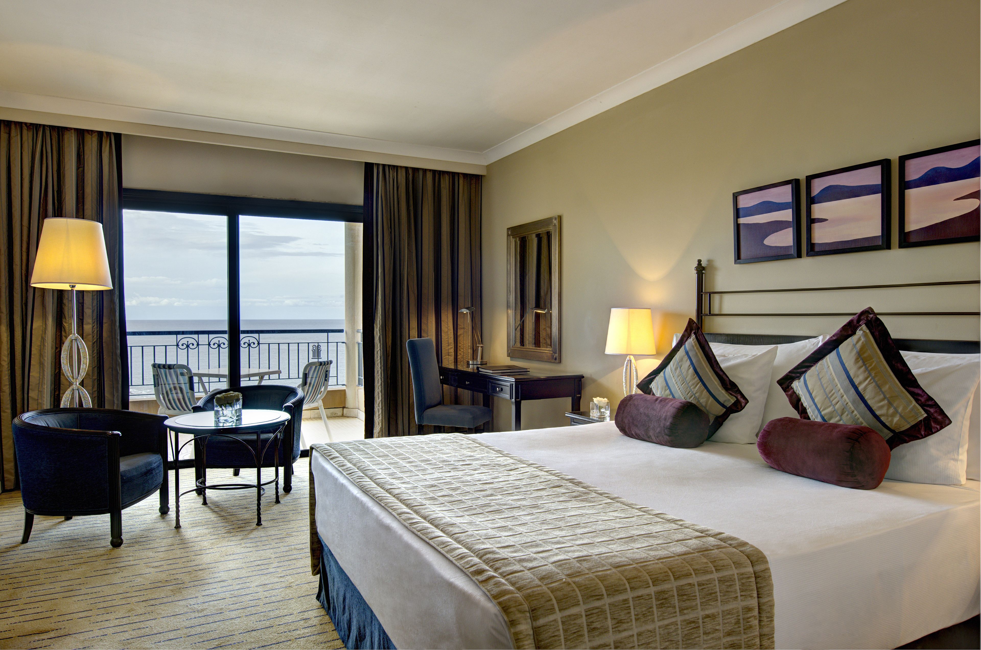 Habitación de hotel con una cama grande, dos sillas, un escritorio y vista al océano.
