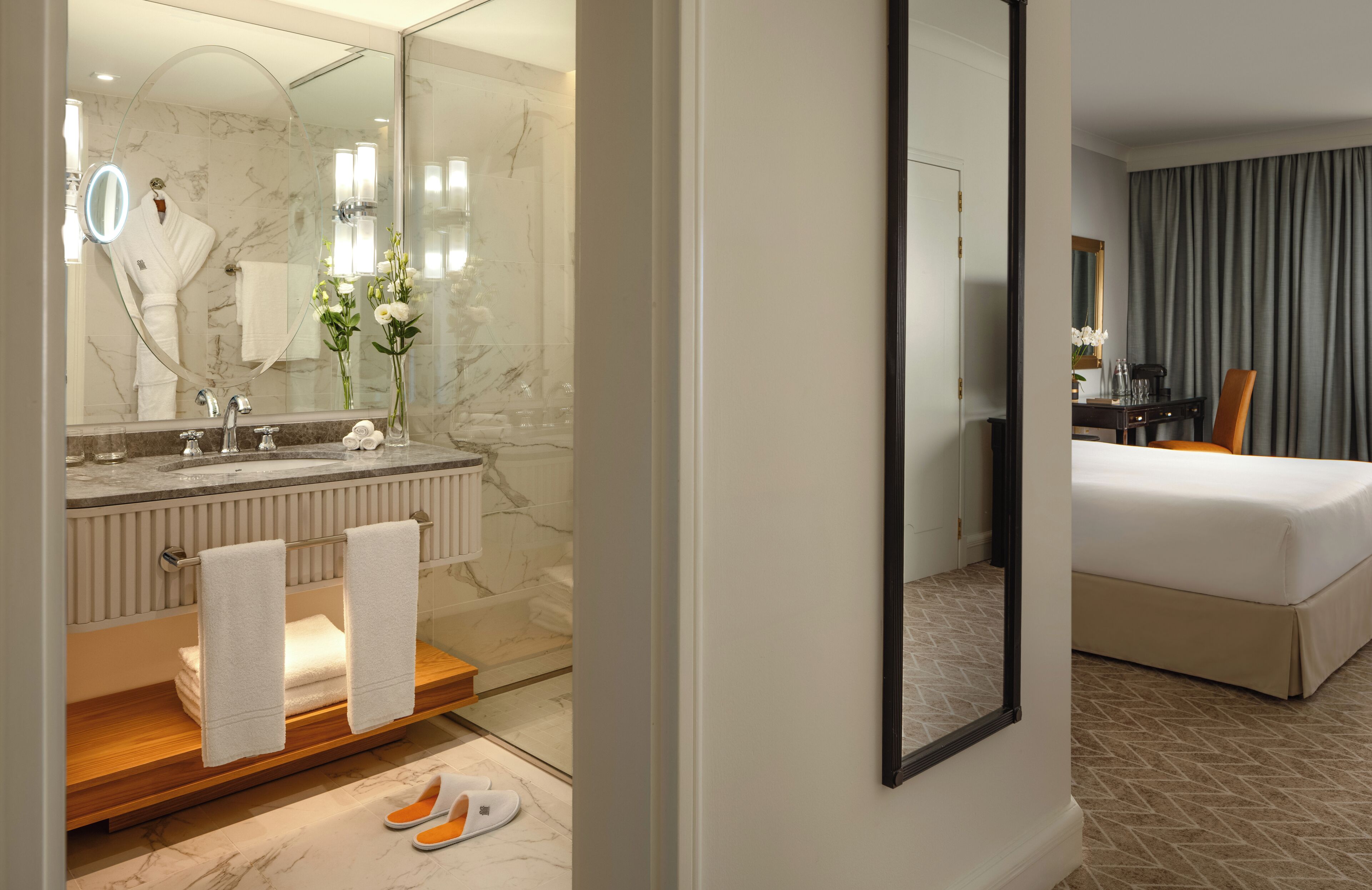 A hotel room with a bathroom featuring a marble sink, a mirror, and a towel rack.