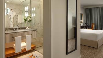 A hotel room with a bathroom featuring a marble sink, a mirror, and a towel rack.