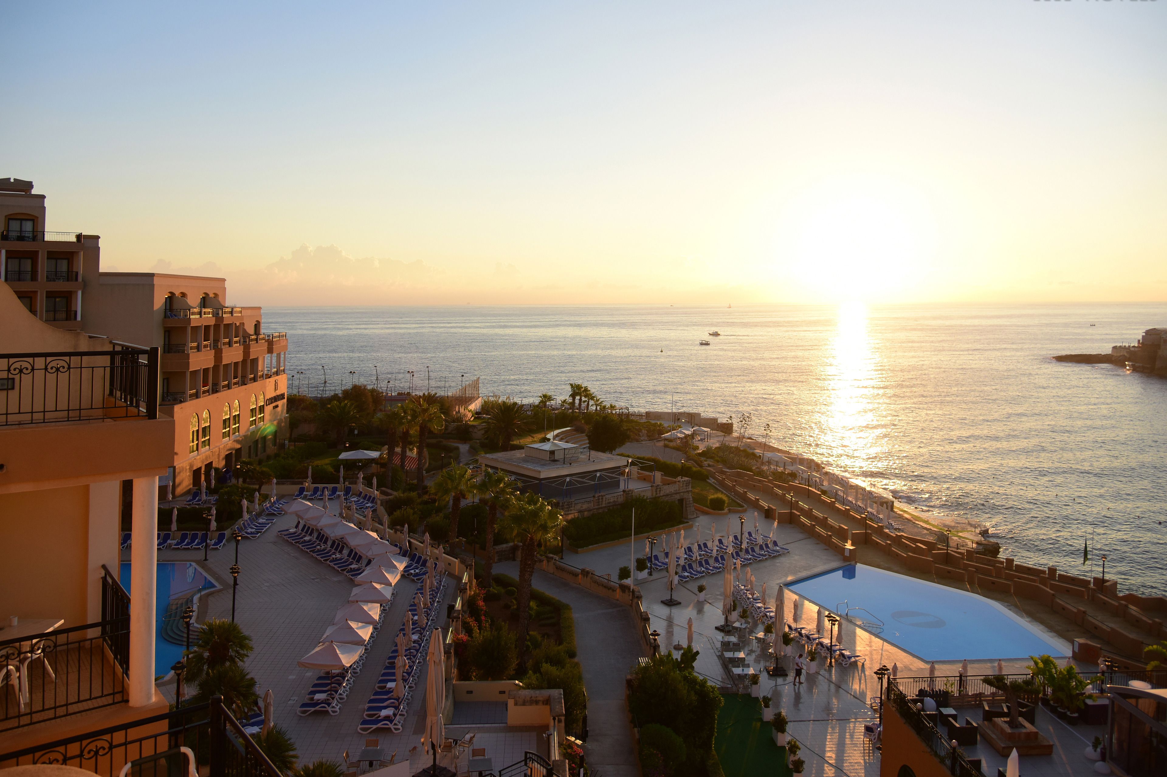 Ein Resort mit Poolbereich, Liegestühlen und Blick auf das Meer bei Sonnenuntergang.