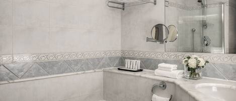 A modern bathroom with a bathtub, a shower, a vanity with a mirror, and a vase with flowers.