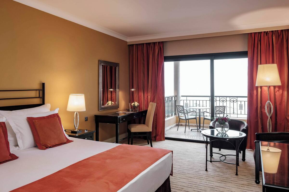 Ein Hotelzimmer mit Bett, Schreibtisch, Stuhl und einem Balkon mit Sitzgelegenheit.