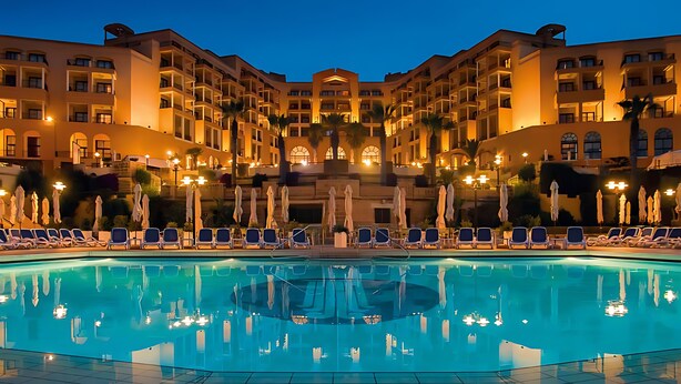 A hotel with a large pool, multiple balconies, and outdoor seating areas. - Corinthia St George's Bay (St. Julian's)