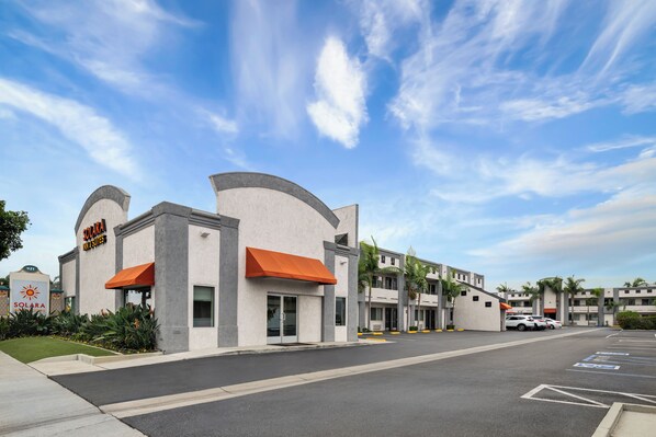 A hotel with a modern design, featuring a curved facade, orange awnings, and a parking lot with marked spaces.