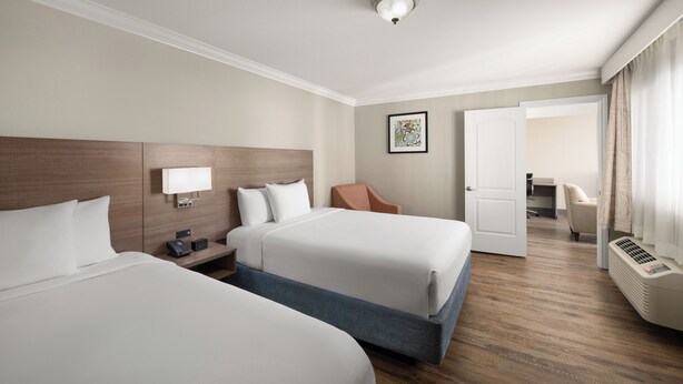 Ein Hotelzimmer mit zwei Betten, einem Schreibtisch, einem Sessel, einem Bild an der Wand und einer Tür zu einem weiteren Raum.