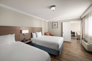 A hotel room with two beds, a desk, a chair, a picture on the wall, and a door leading to another room. - Solara Inn and Suites (Anaheim)