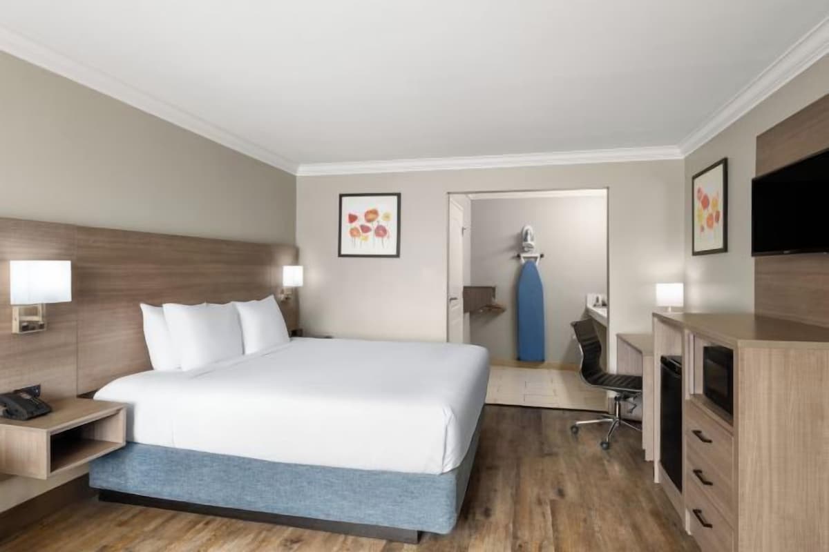 A hotel room with a bed, bedside tables, a desk, a chair, a TV, and a bathroom visible through an open door.