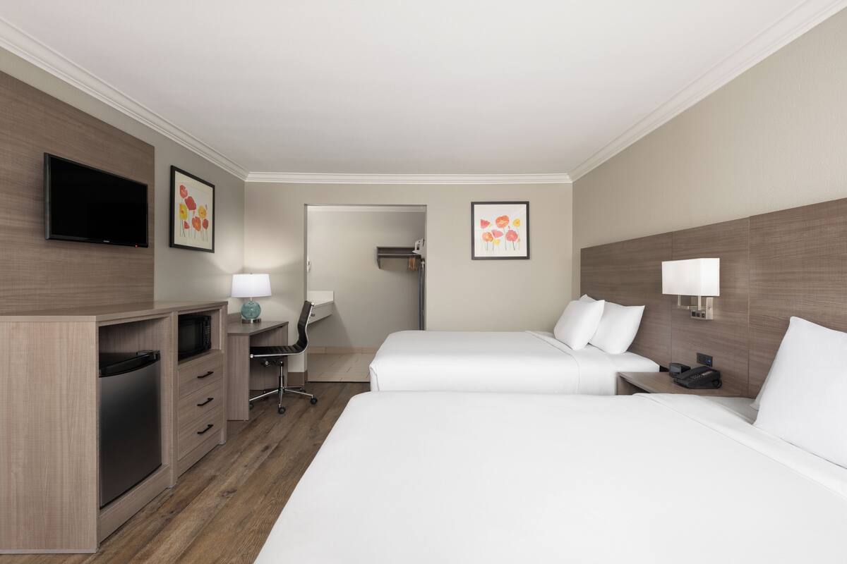 A hotel room with two beds, a desk, a chair, a television, and artwork on the walls.