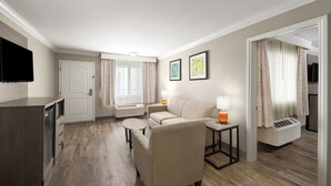 Ein modernes Hotelzimmer mit einer Couch, einem kleinen Tisch, einem Fernseher und einer Waschgelegenheit.