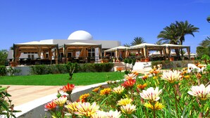 A hotel with outdoor seating areas, a large dome structure, and a well-maintained garden with colorful flowers. - Djerba Plaza Thalasso & Spa (Djerba Midun)