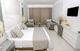 Habitación de hotel con una cama grande, dos camas más pequeñas, un escritorio, un televisor y una ventana con cortinas.