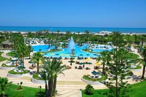 Un resort con piscina central, numerosas tumbonas y palmeras.