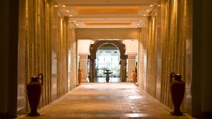 A corridor with a tiled floor, flanked by columns and large vases, leading to a doorway with a glass door. - Djerba Plaza Thalasso & Spa (Djerba Midun)