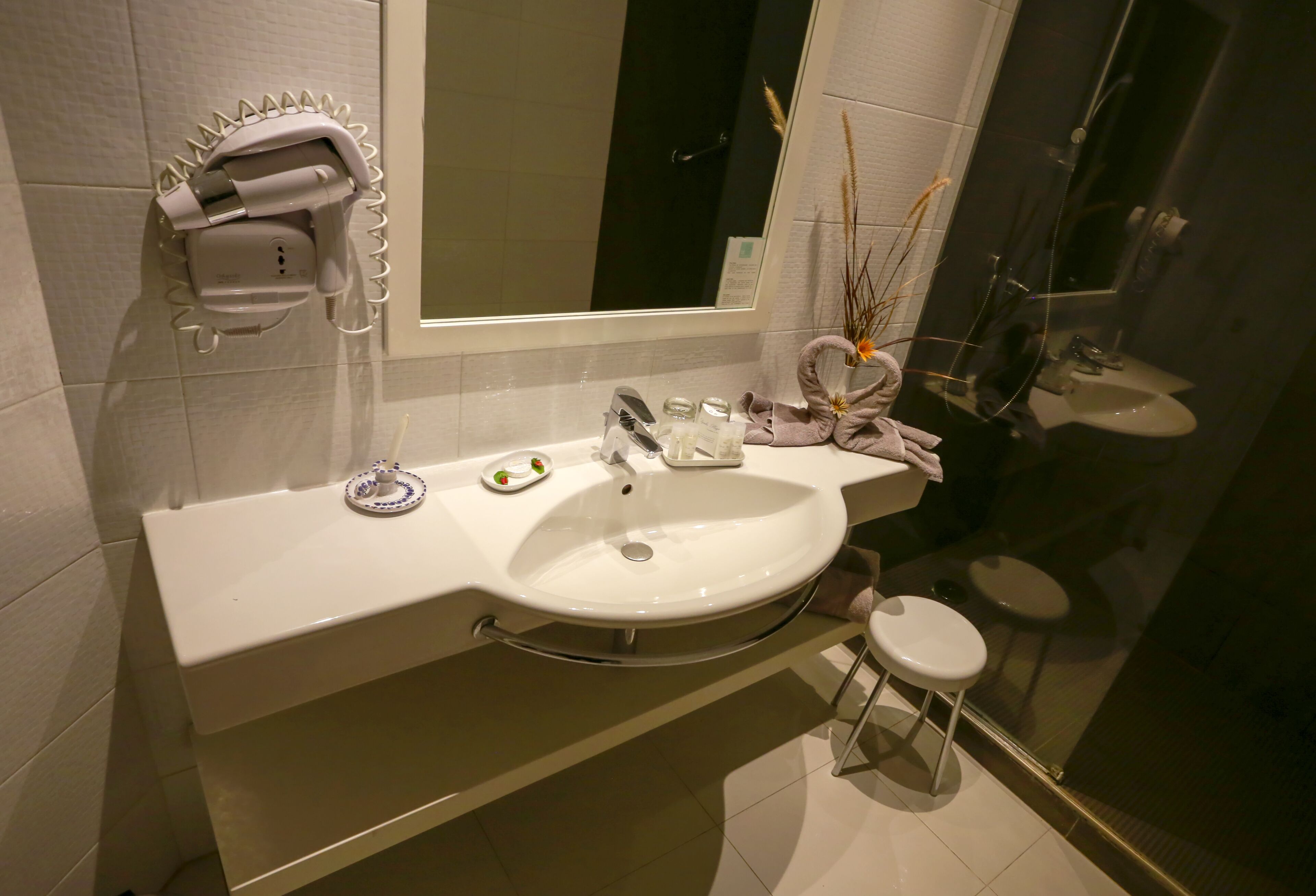 Ein modernes Badezimmer mit einem weißen Waschbecken, einem Spiegel, einem Handtuchhalter und einem kleinen Hocker.