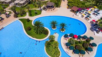 Vista aérea de um resort com uma piscina central ampla, rodeada por palmeiras e espreguiçadeiras.