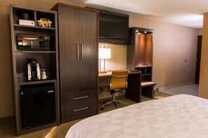 A hotel room with a bed, a desk with a chair, a wardrobe, a television, and a coffee machine.