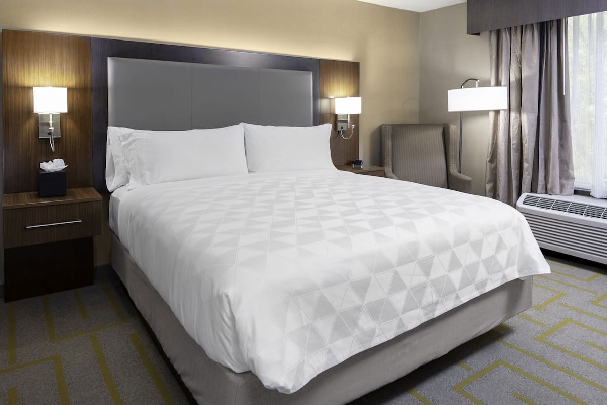 A hotel room with a large bed, bedside lamps, a chair, a desk, and a window with curtains.