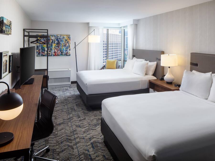 Ein Hotelzimmer mit zwei Betten, einem Schreibtisch, einem Sessel, einem Fernseher und Bildern an den Wänden.