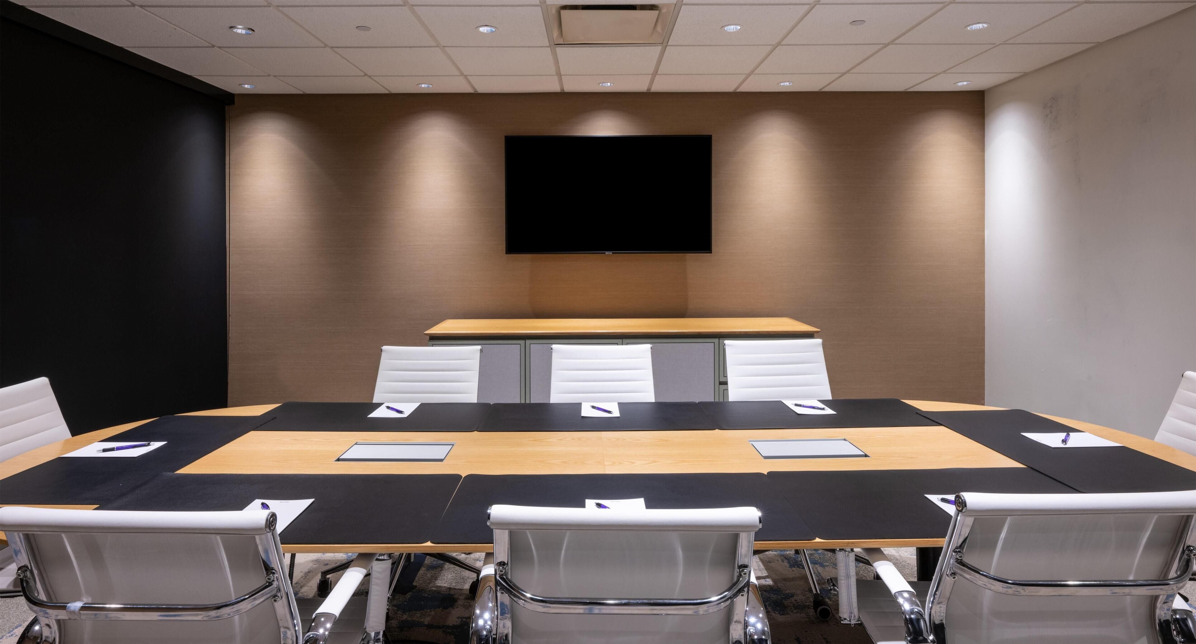 Un salón de conferencias con una gran mesa, sillas, un televisor de pantalla plana y un panel de pared de madera.