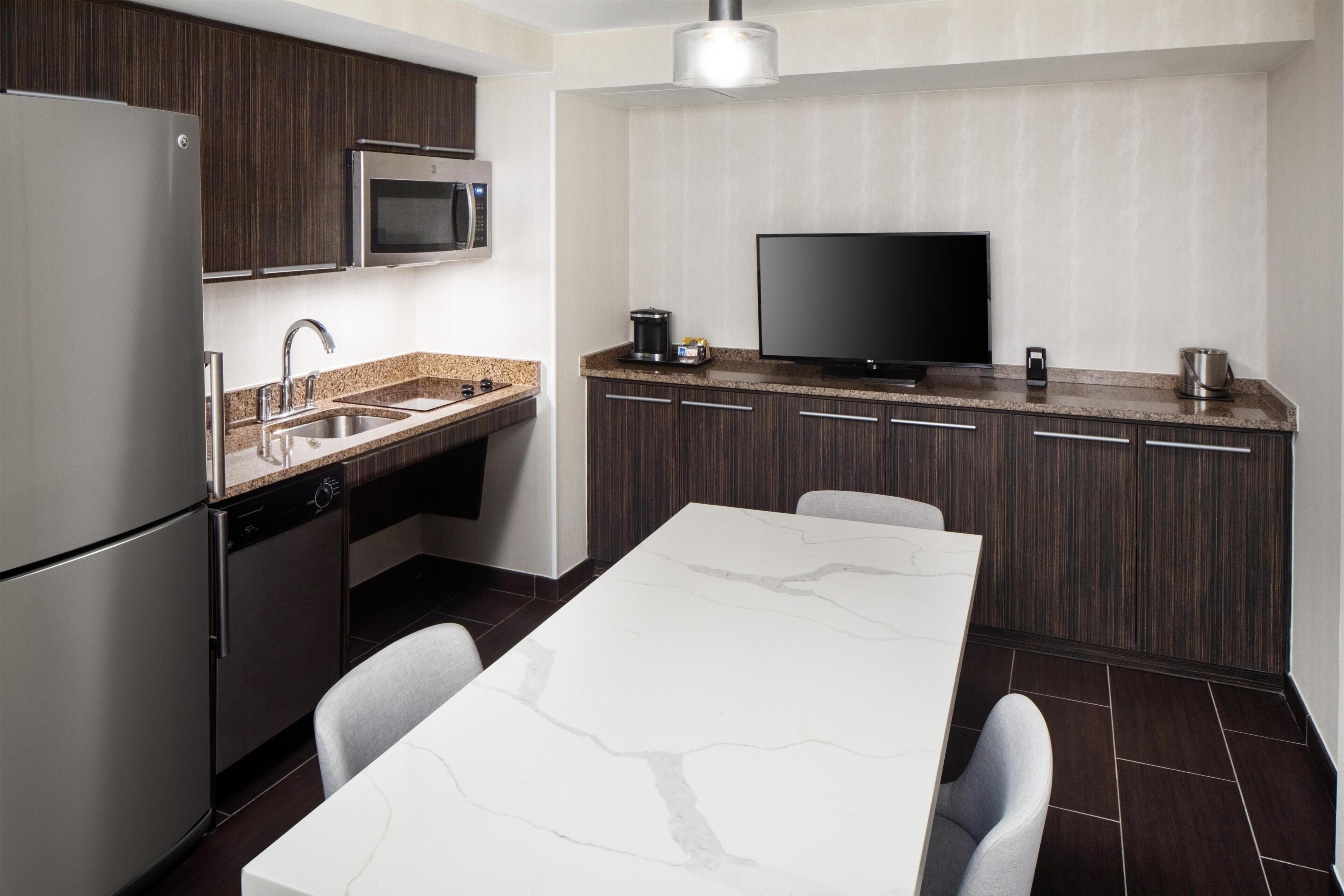 A modern kitchen with a built-in microwave, stainless steel refrigerator, and a flat-screen TV.