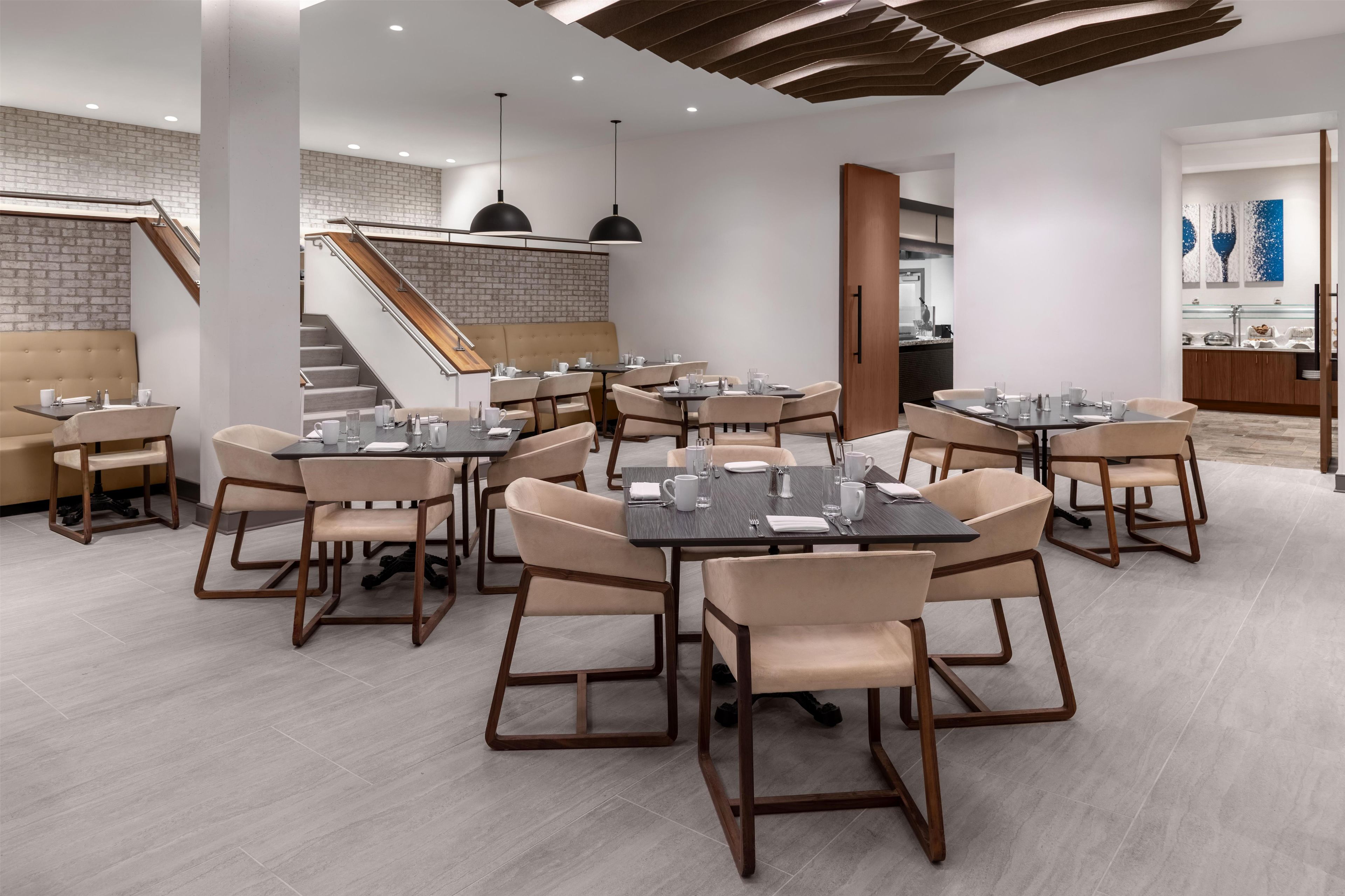 A modern restaurant with multiple dining tables and chairs, a staircase, and a buffet area.