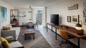A modern hotel room with a sofa, a desk, a TV, a dining area, and a view of the city. - The Bethesdan Hotel, Tapestry Collection by Hilton (Bethesda)