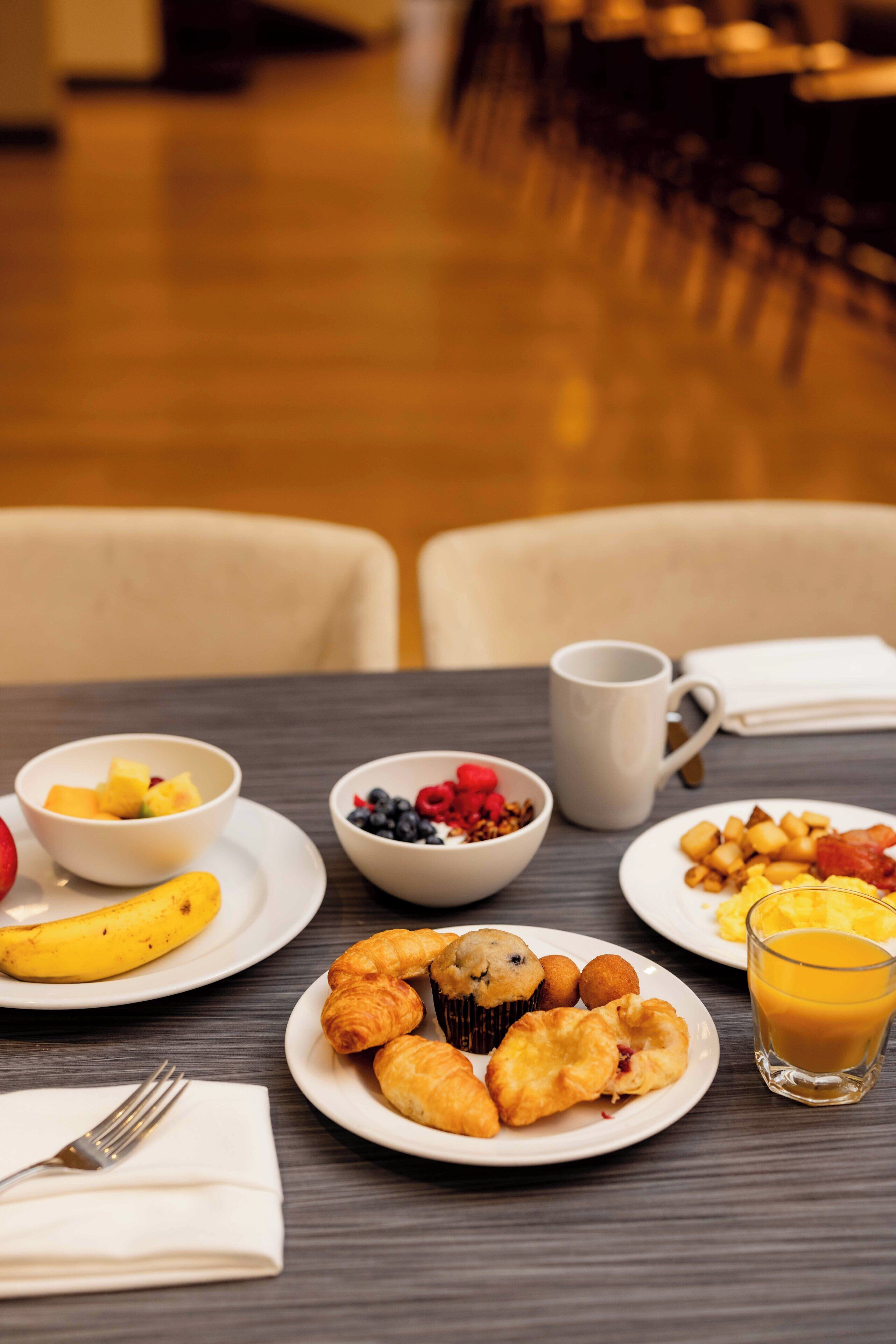 A breakfast setting with plates of food, a coffee mug, and a glass of orange juice on a table.