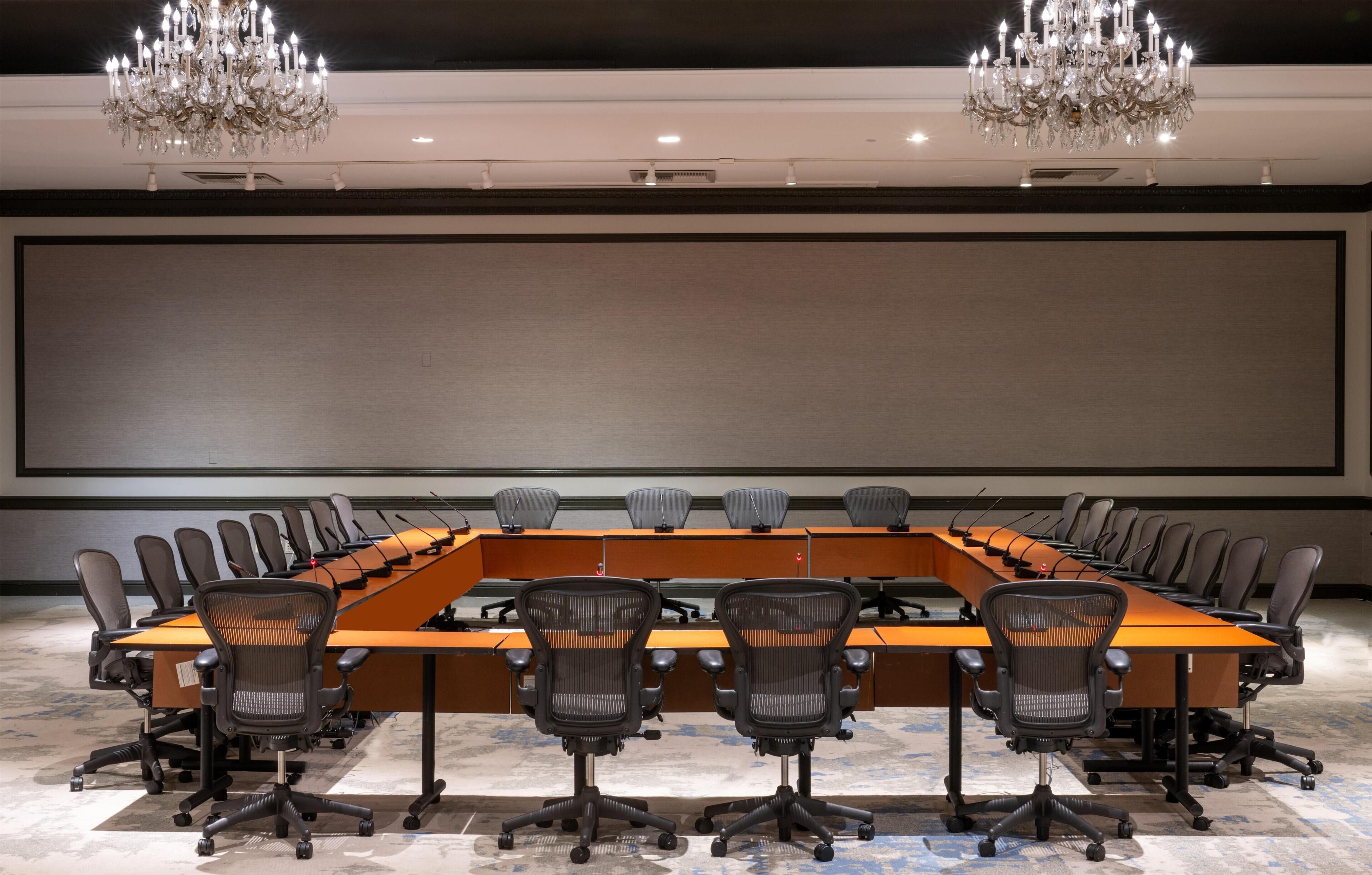 A conference room with a long table, multiple chairs, a large screen, and chandeliers.