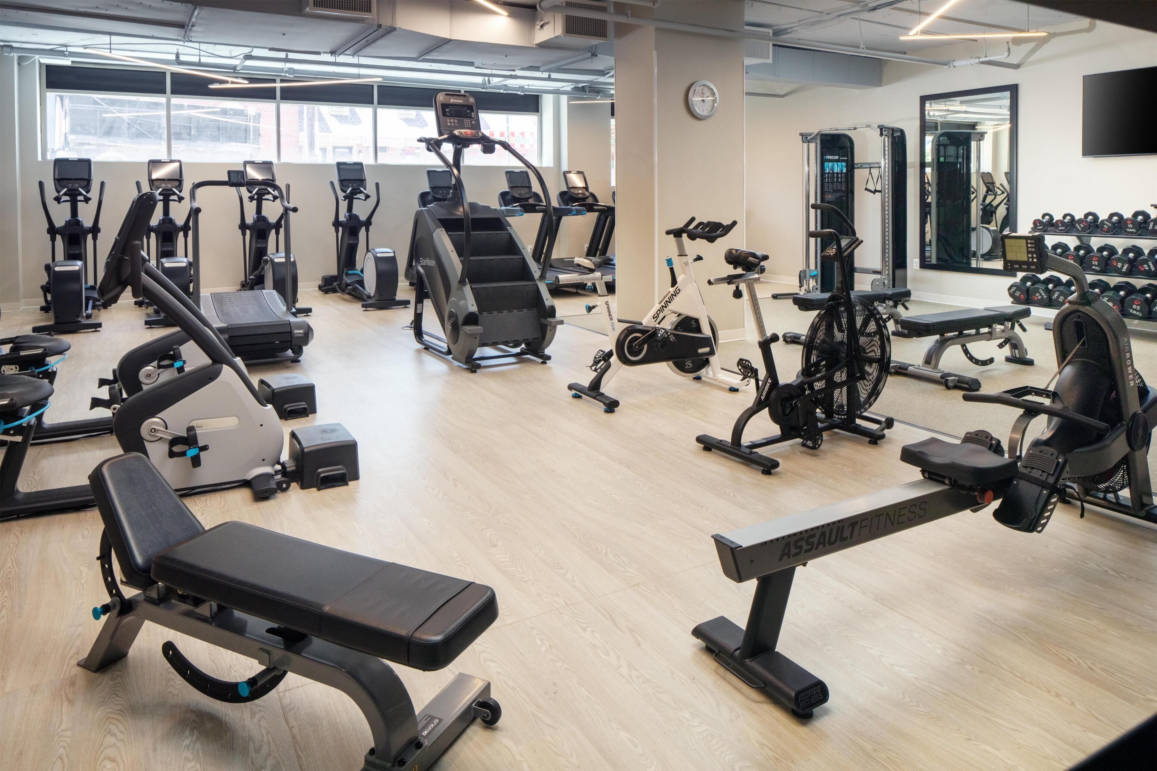 Un gimnasio con diferentes equipos de ejercicio, incluyendo cintas de correr, bicicletas estáticas y máquinas de pesas.
