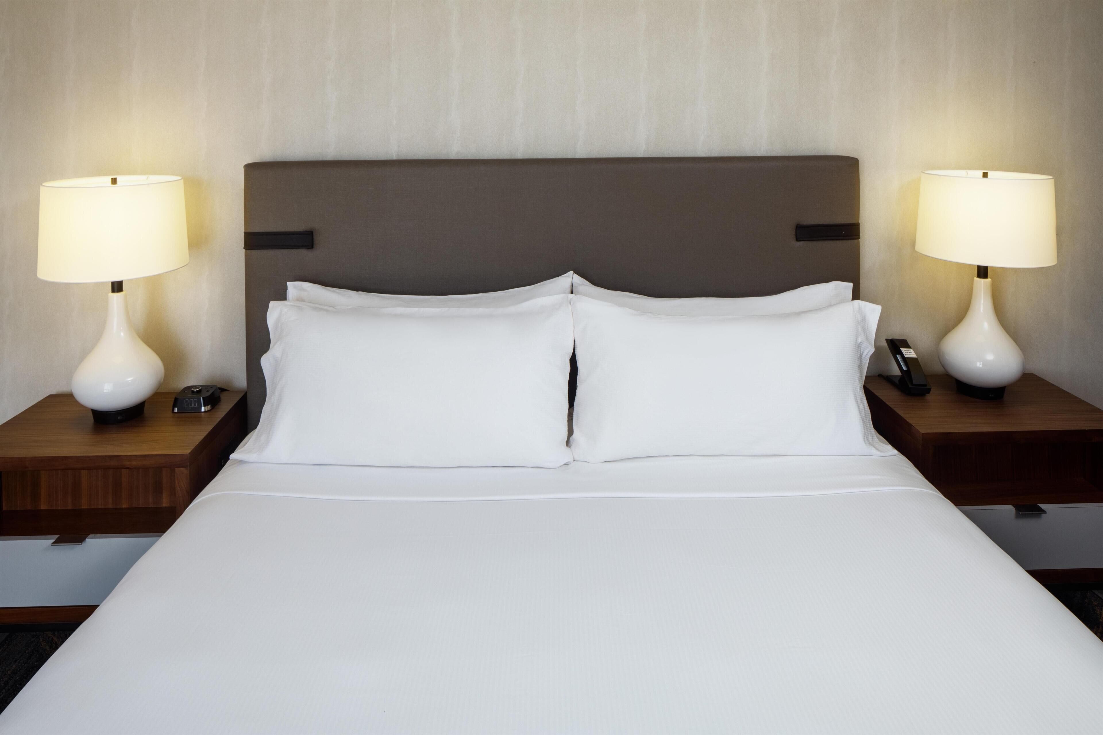 Une chambre d’hôtel avec un grand lit, deux tables de chevet avec des lampes et une tête de lit.