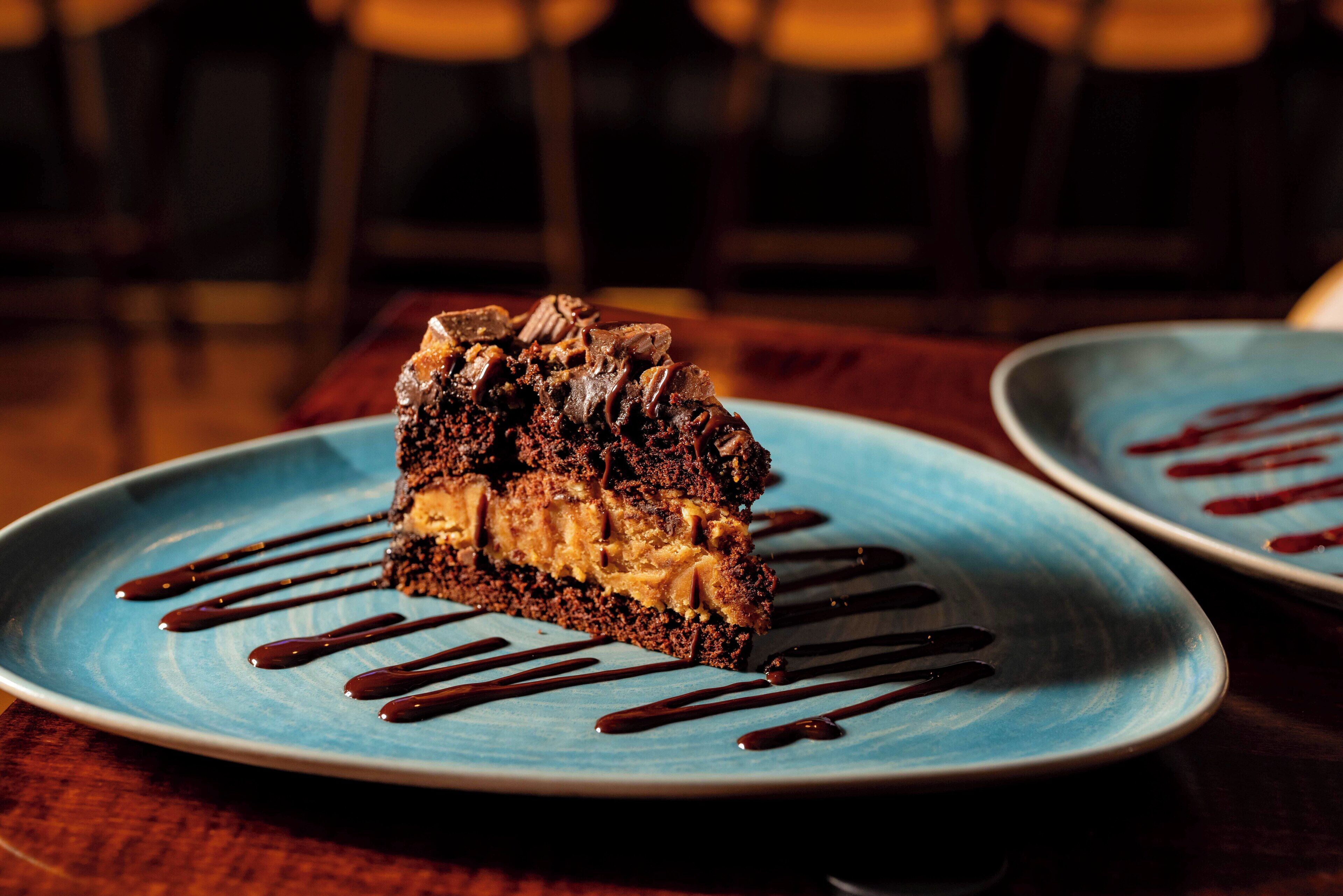 Una porción de pastel en un plato azul con salsa de chocolate.