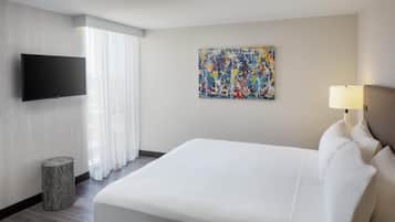 A hotel room with a bed, a flat-screen TV, a painting on the wall, and a lamp.