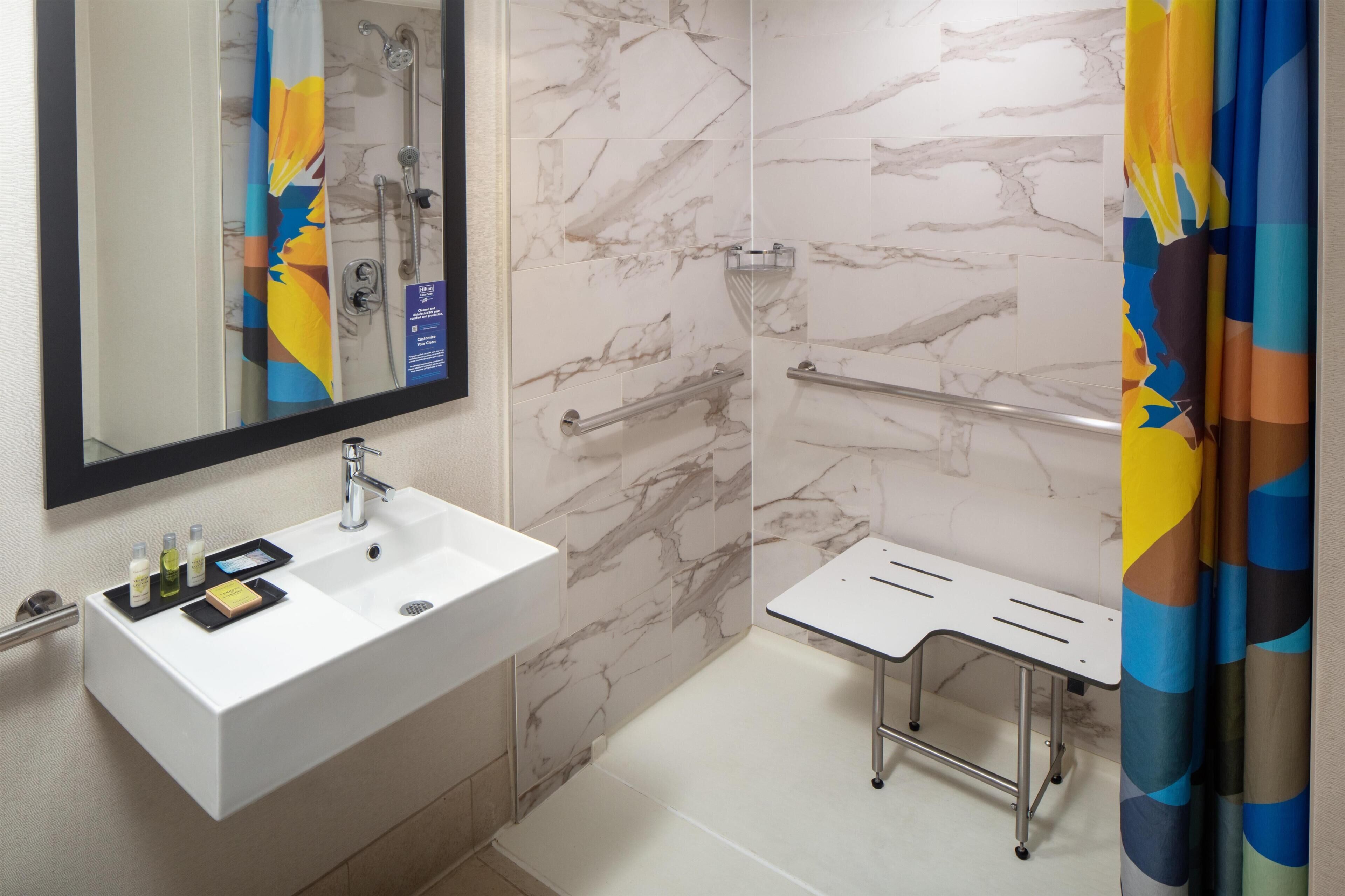 Een badkamer met een wit wastafelmeubel, spiegel, douche en een bankje.
