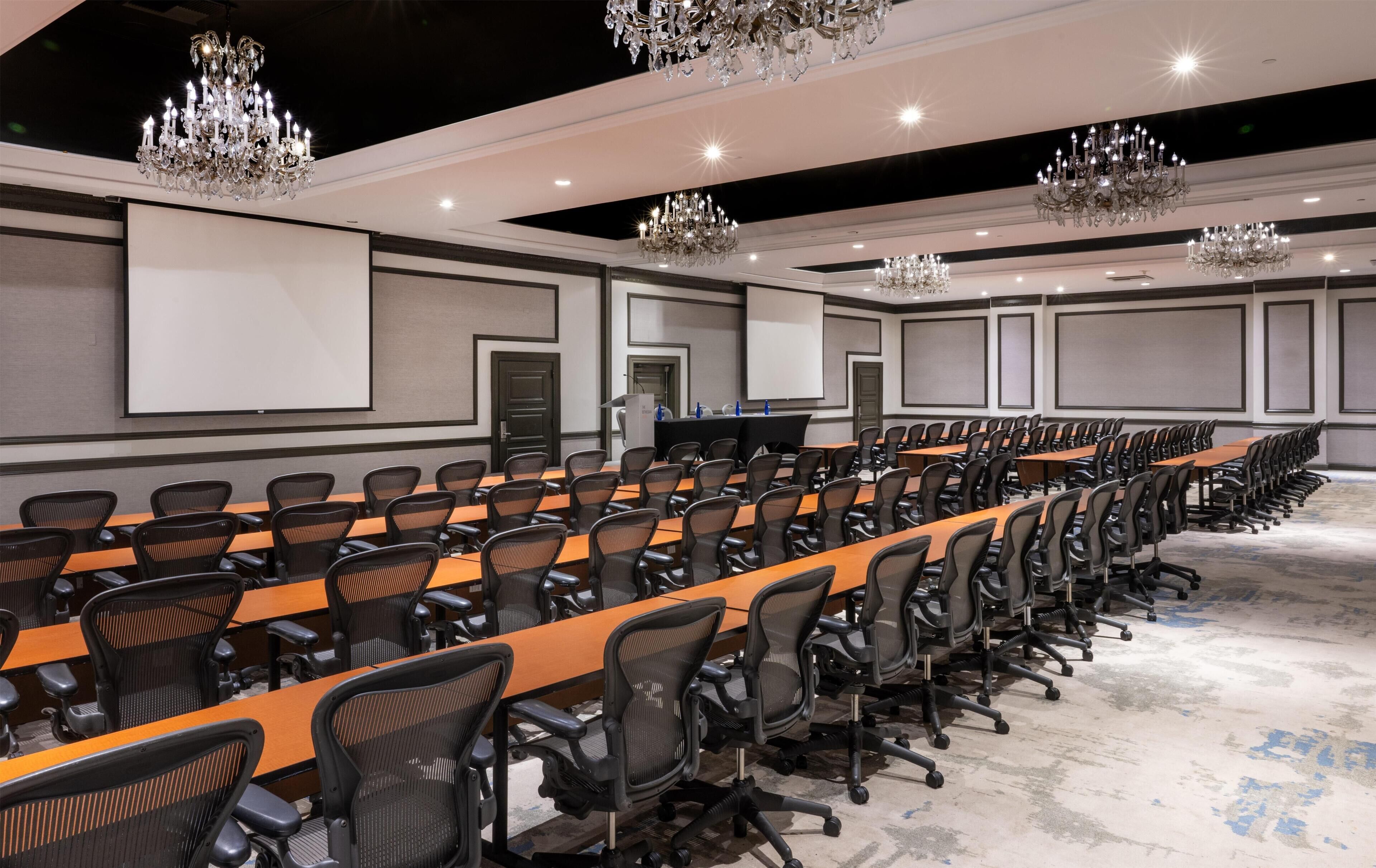 A conference room with long tables, chairs, a podium, and a projector screen.