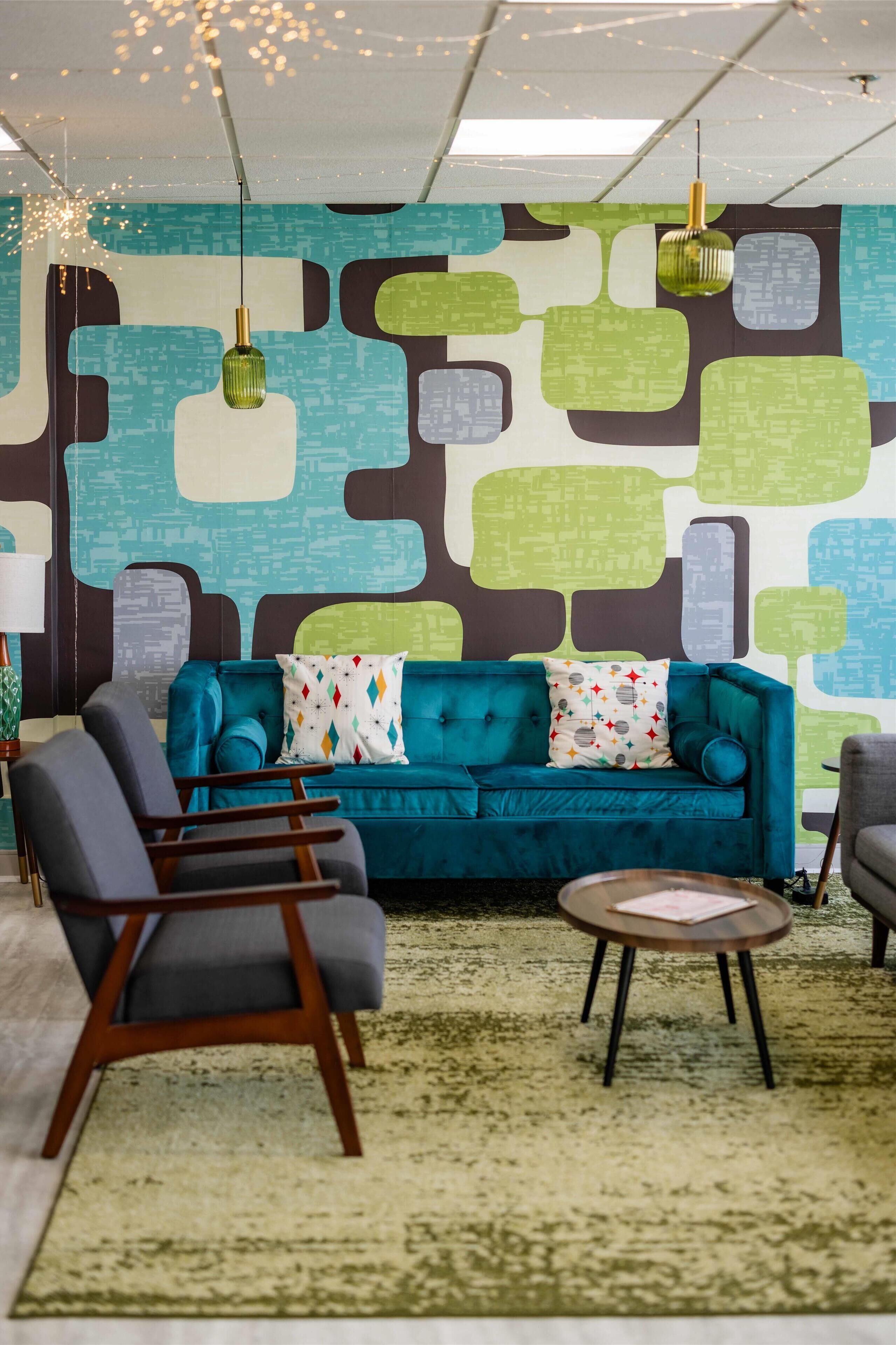 A room with a teal sofa, a round coffee table, and a patterned wall.