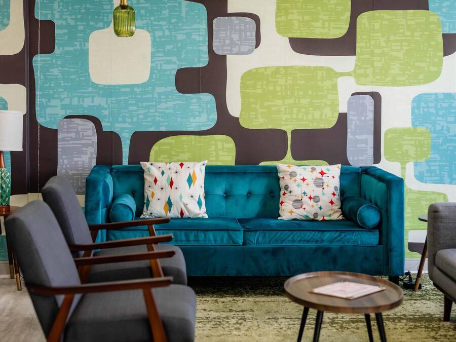A room with a teal sofa, a round coffee table, and a patterned wall.