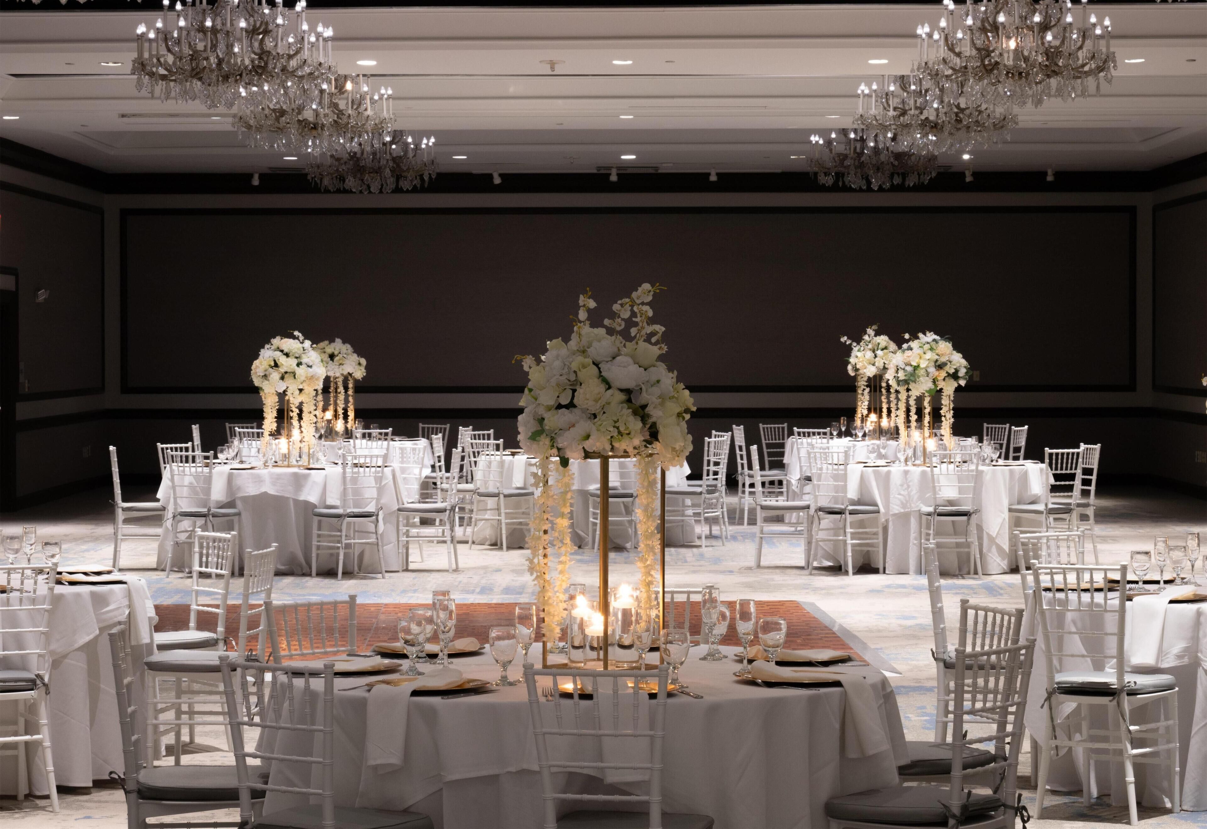 Un salón de banquetes con mesas redondas, sillas blancas y candelabros.
