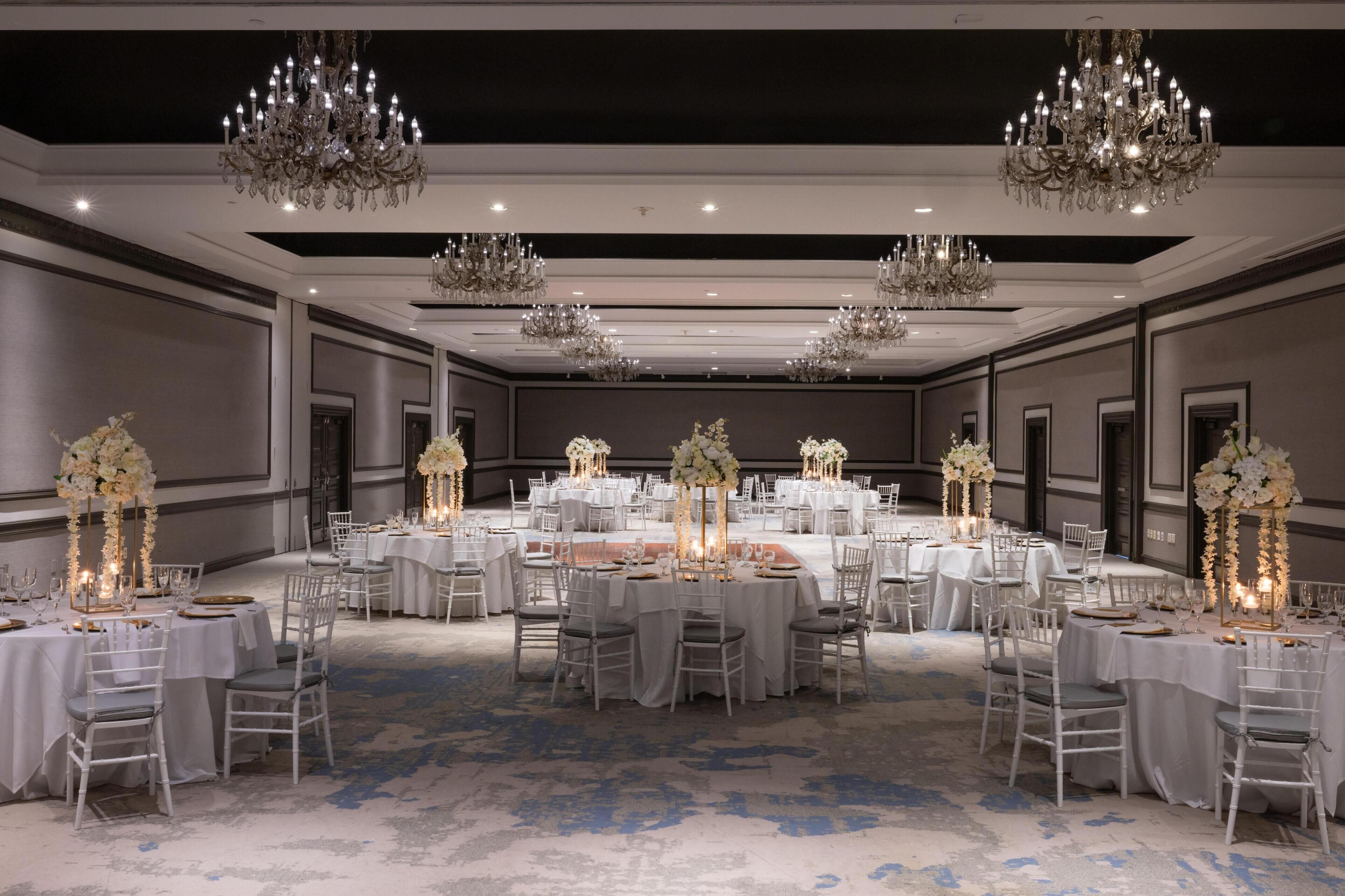Un amplio salón de banquetes con varias mesas redondas, sillas blancas y candelabros.
