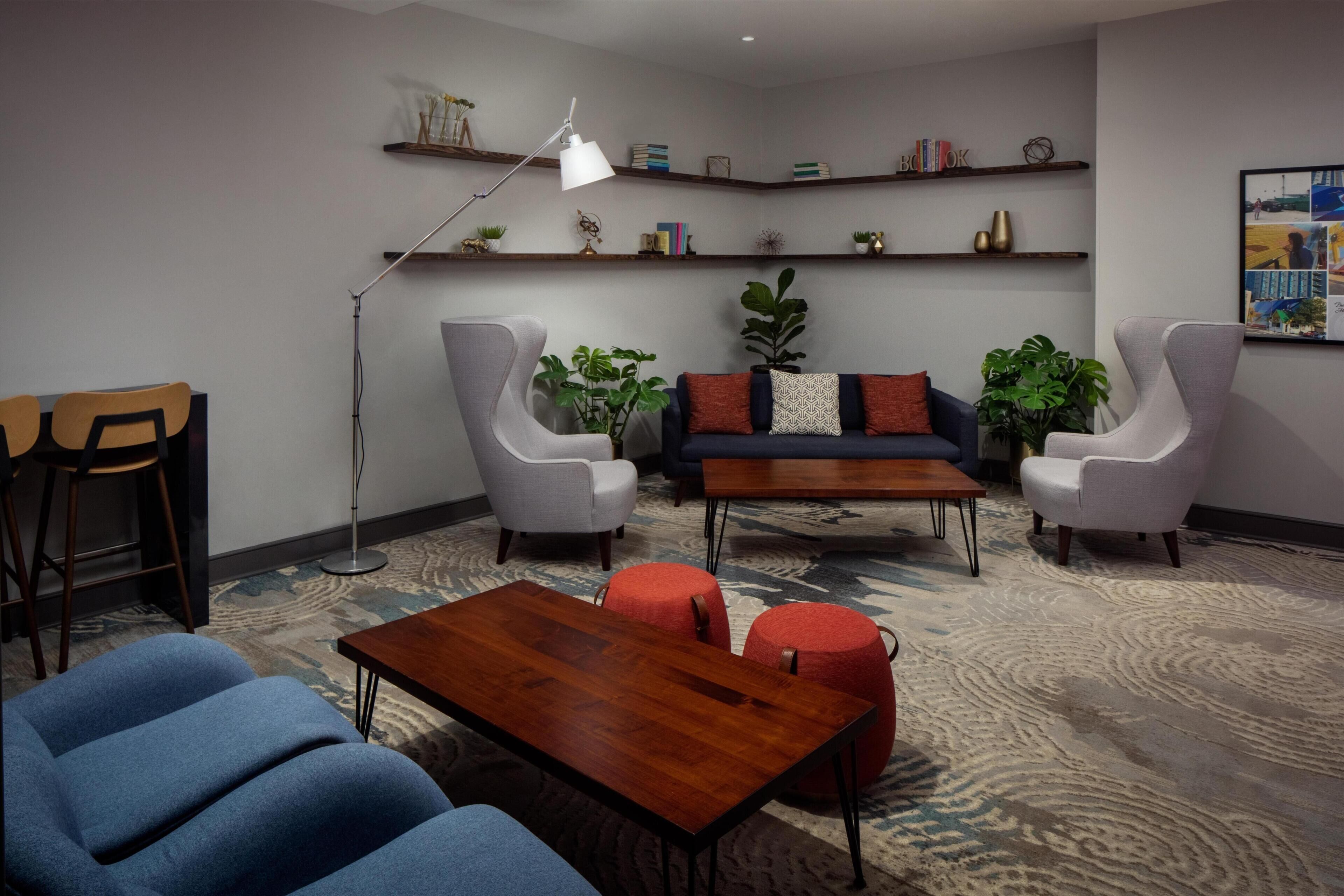 A modern living room with a sofa, two armchairs, a coffee table, and a floor lamp. There are shelves with books and decorative items on the wall.
