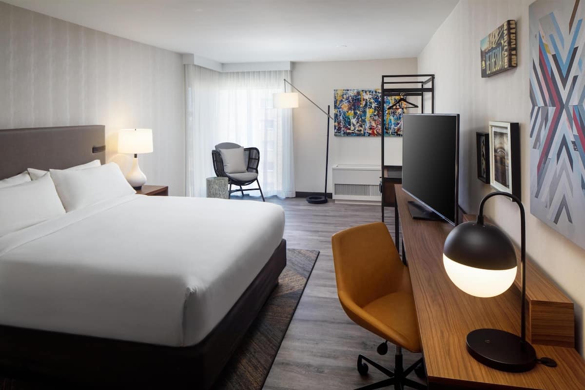 Et hotelværelse med en stor seng, et skrivebord med stol, et fjernsyn og kunst på væggene.