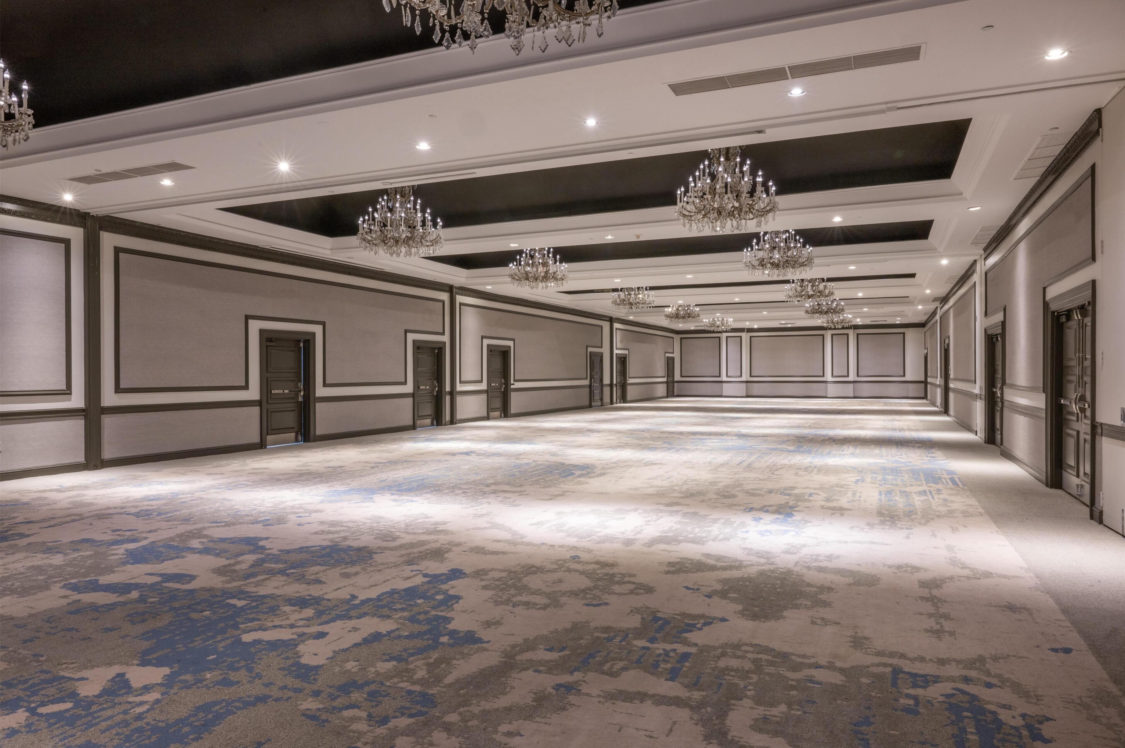 Un amplio vestíbulo de hotel con alfombra estampada, varias puertas y candelabros.