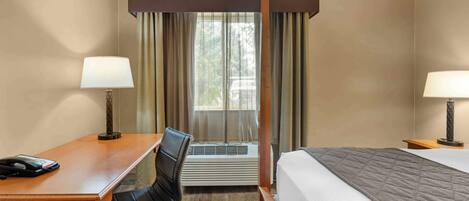A hotel room with a bed, a desk with a telephone, a chair, an air conditioning unit, and two lamps.