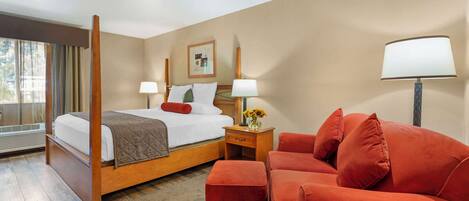 Une chambre d’hôtel avec un lit à baldaquin, un canapé rouge, une petite table sur laquelle est posé un vase de fleurs, et une fenêtre avec des rideaux.