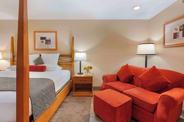 A hotel room with a bed, a red sofa, a nightstand with a lamp, and framed pictures on the wall. - Best Western Prineville Inn (Prineville)
