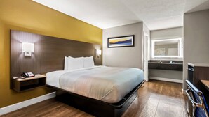 Une chambre d’hôtel avec un lit, une table de chevet, une lampe fixée au mur et un tableau.